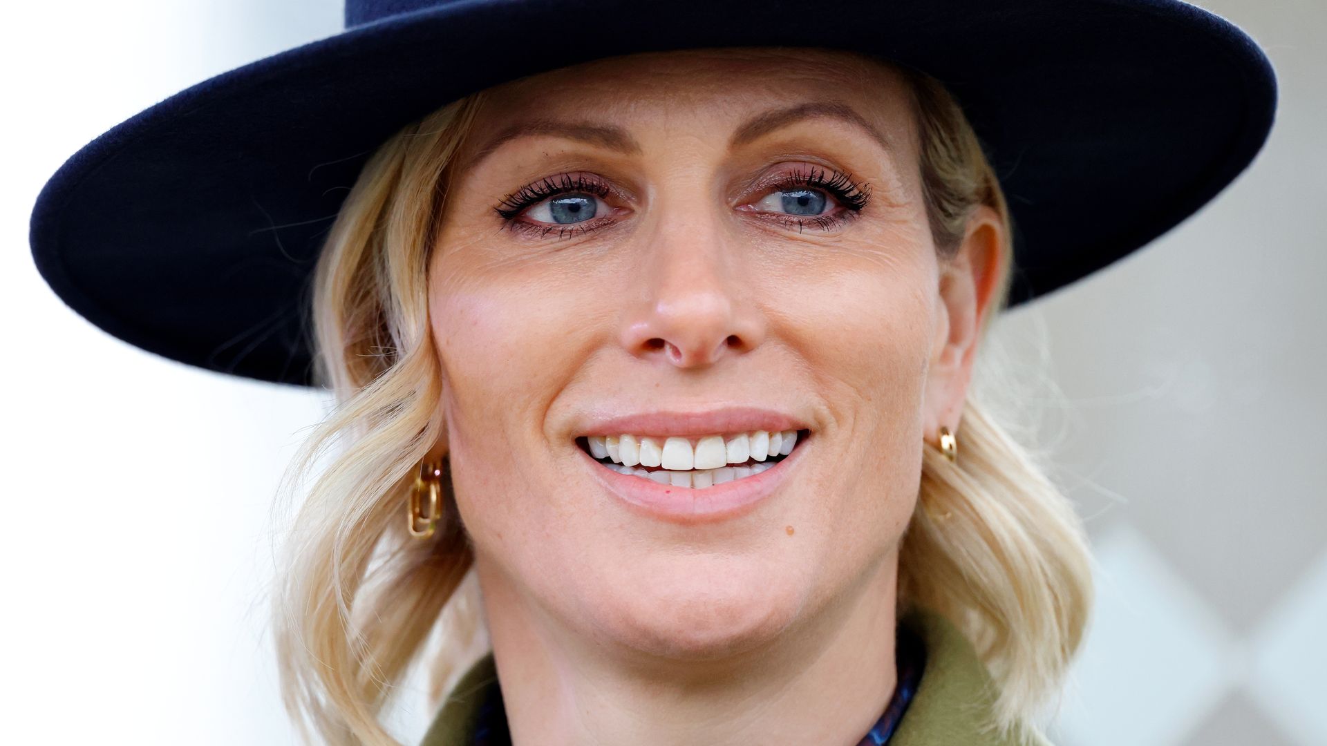 Zara Tindall smiling in a green jacket and blue hat