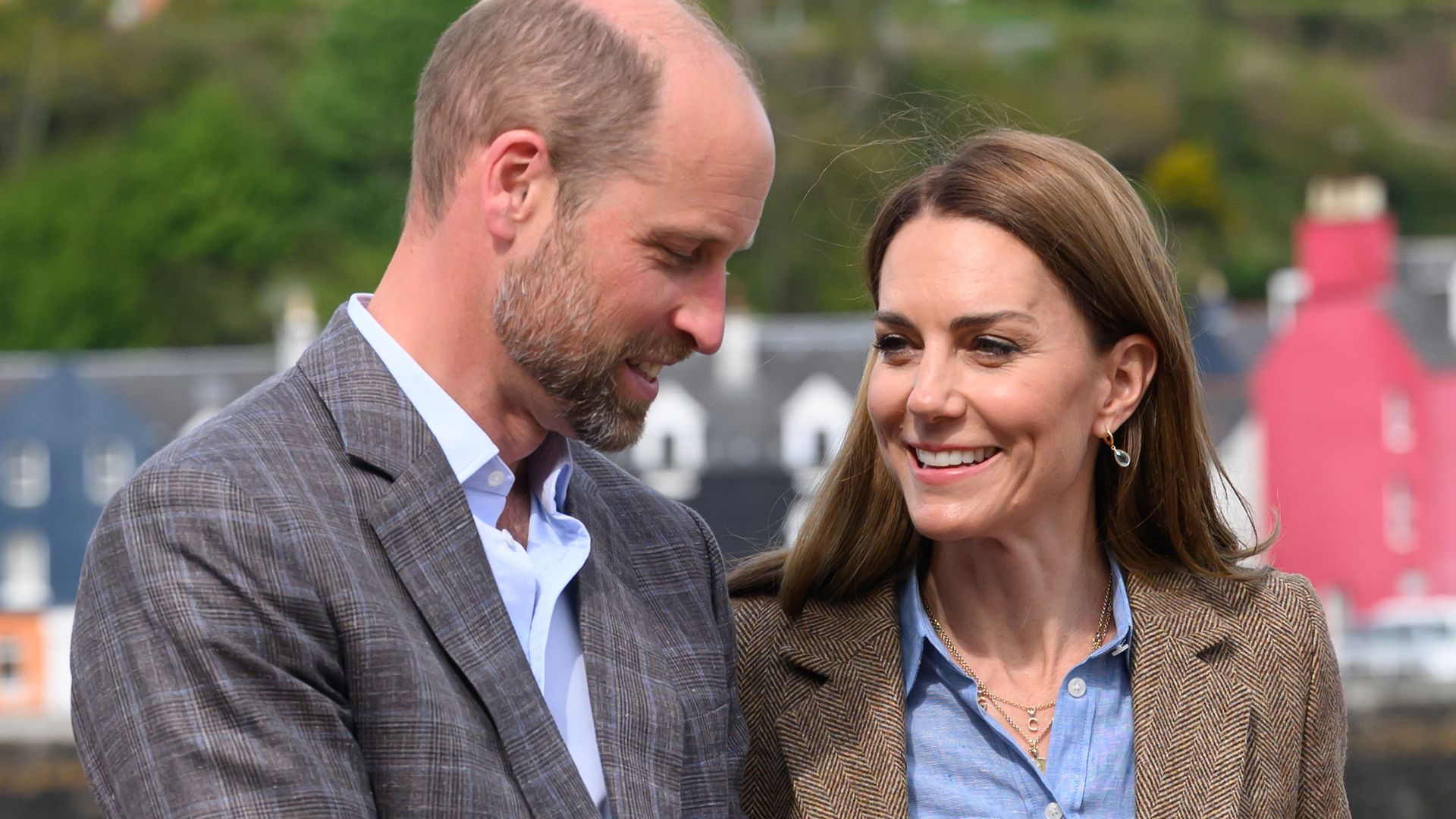 Princess Kate in a blue shirt smiling at William in front of coloured houses