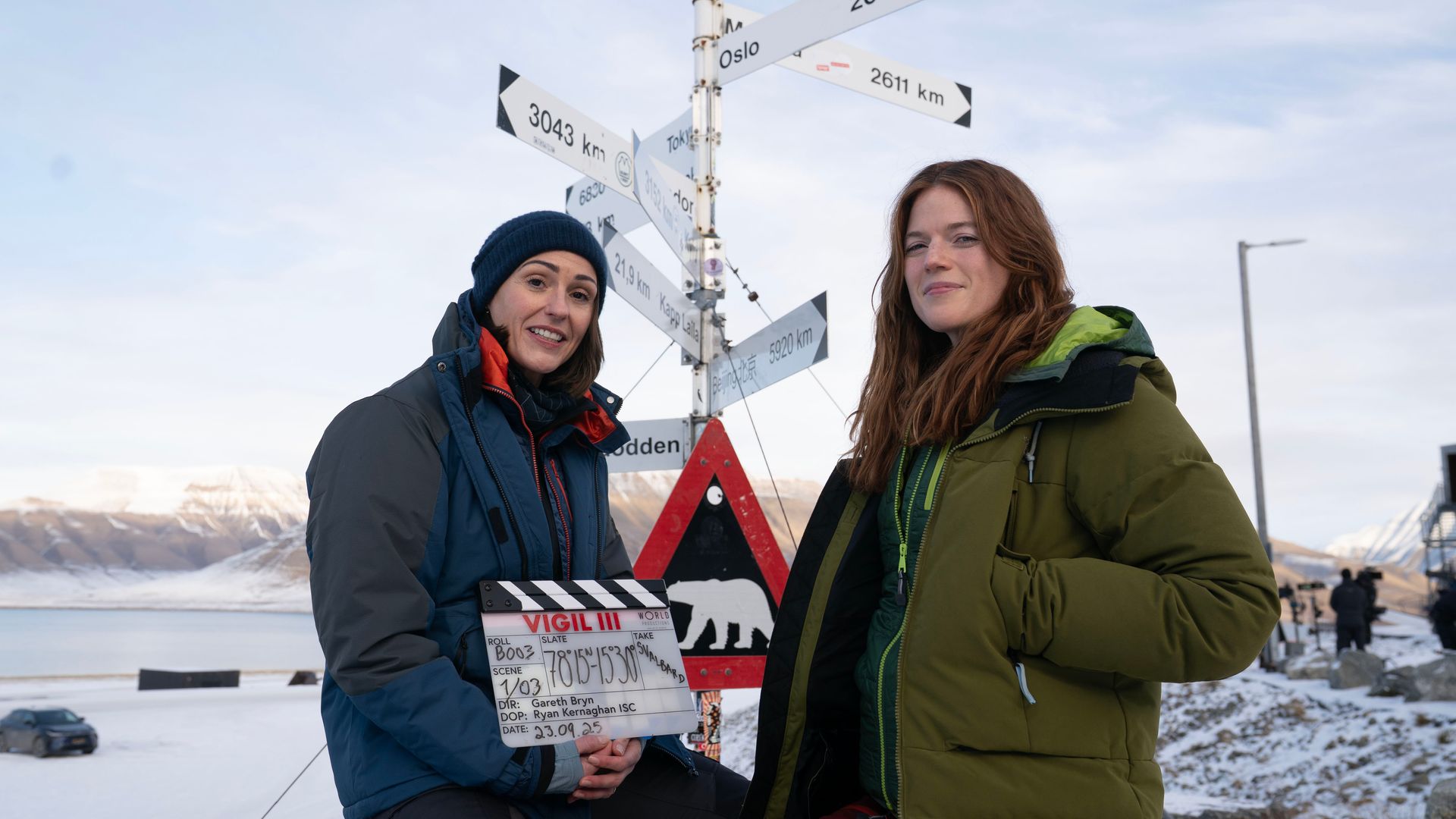 Two women stand with a clapperboard in snow