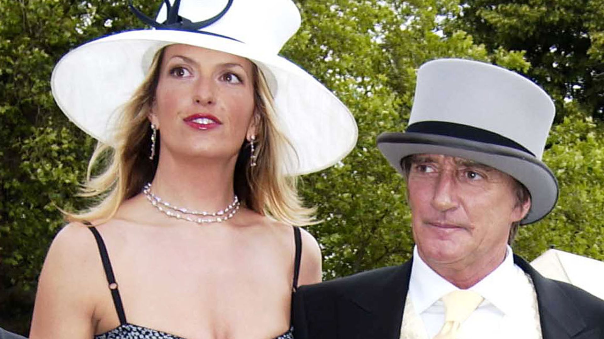 Penny Lancaster in a strappy black dress and a white hat with Rod Stewart in a suit