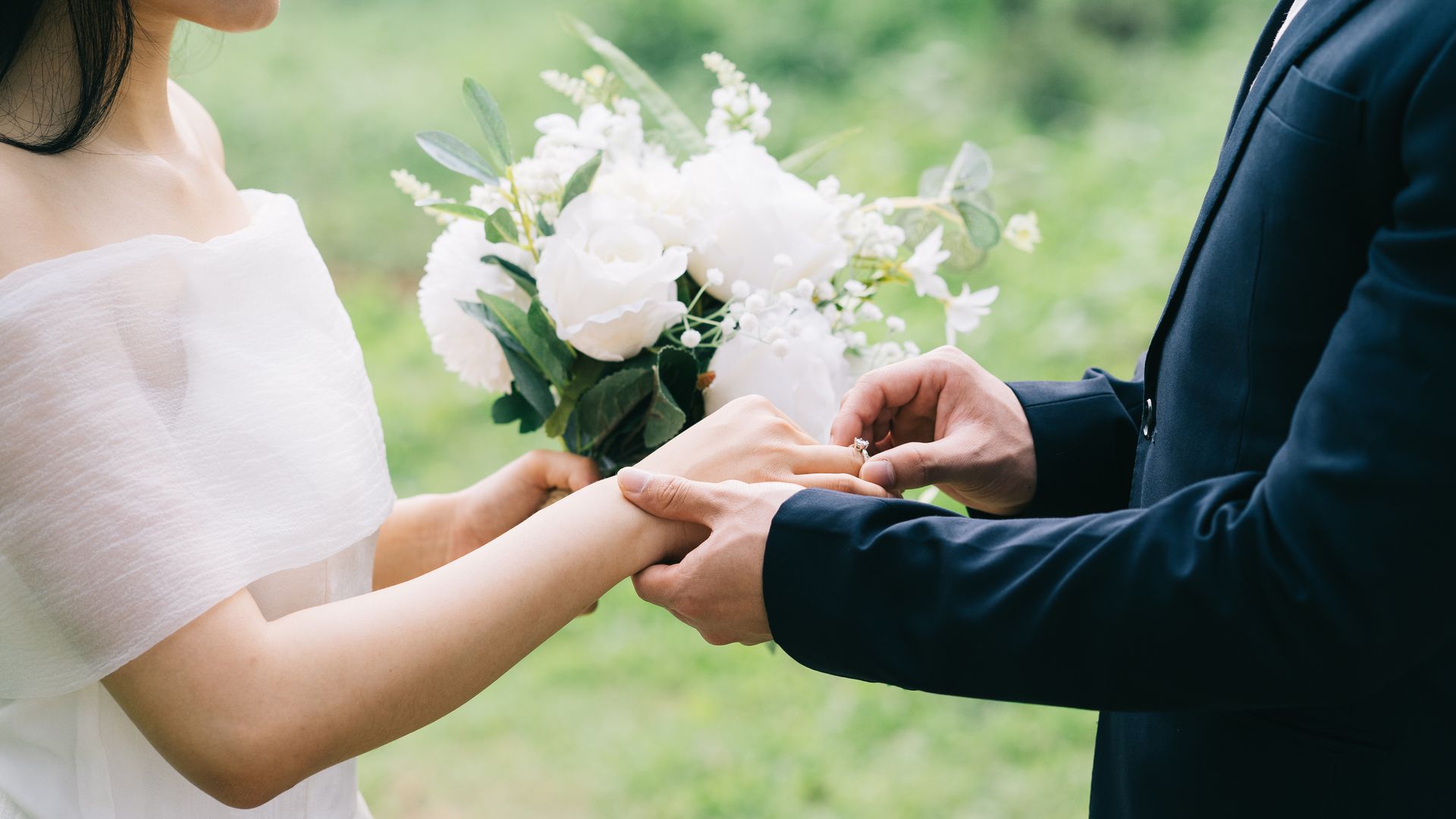 Groom putting ring on bride's finger outside