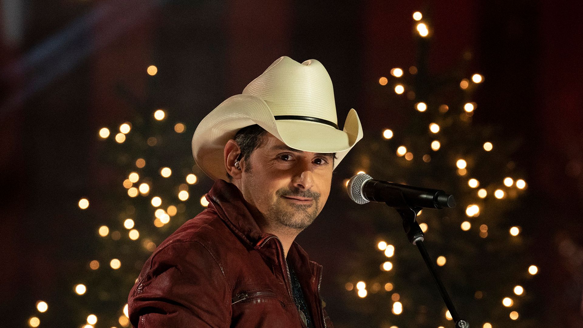 Brad Paisley holds his guitar in front of a Christmas tree