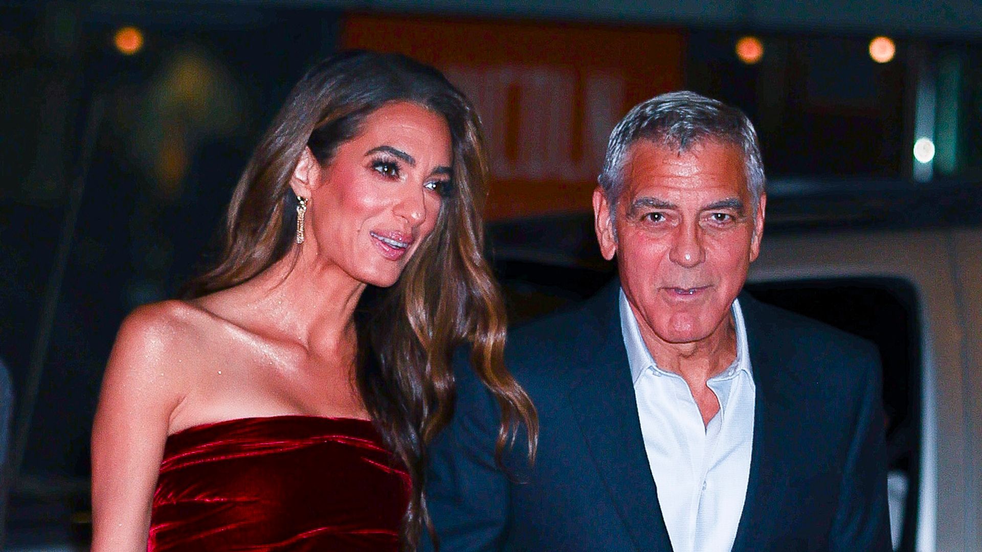 Amal Clooney in red dress and George Clooney in navy suit walking hand in hand 