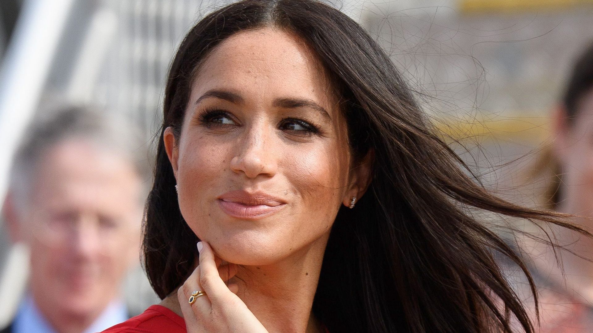 Meghan, Duchess of Sussex looking sideaways with windswept hair in red dress