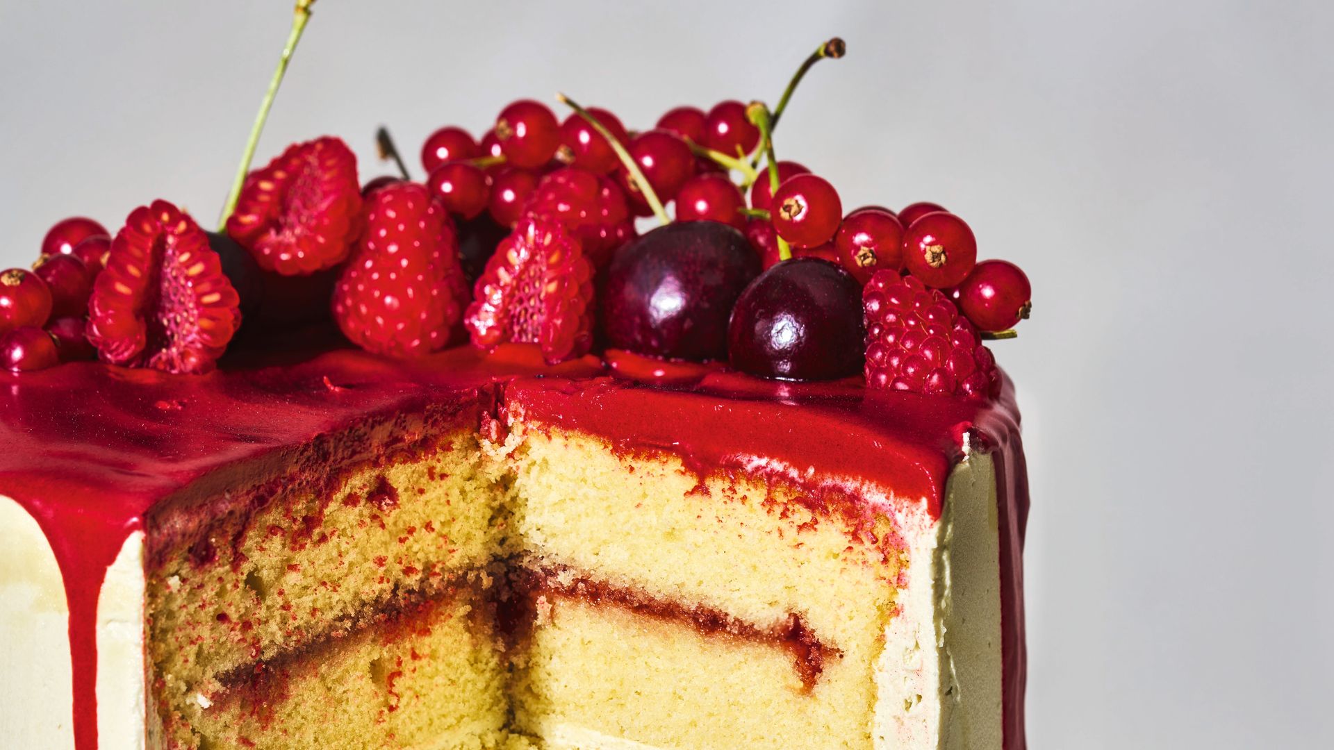 A drip cake with madeina cake and vanilla buttercream topped with cherries and strawberries