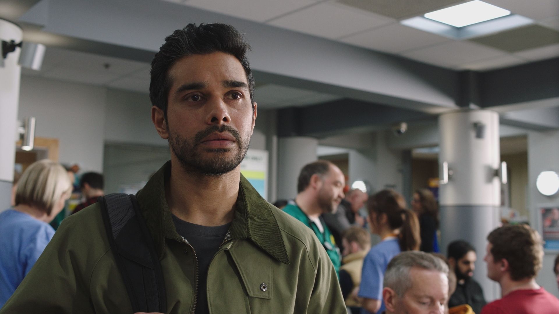 Neet Mohan as Rash Masum standing in an emergency room in Casualty