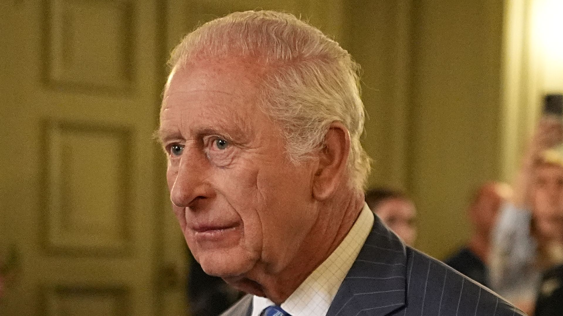King Charles walking through a building with a sullen expression on his face