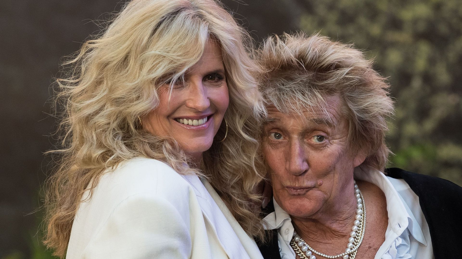 Penny Lancaster in a white blazer smiling with Rod Stewart