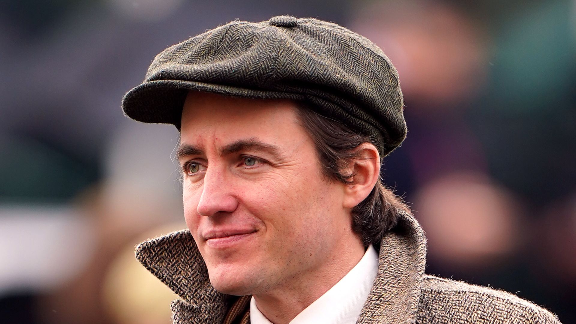 man at races in longline coat and flat cap 