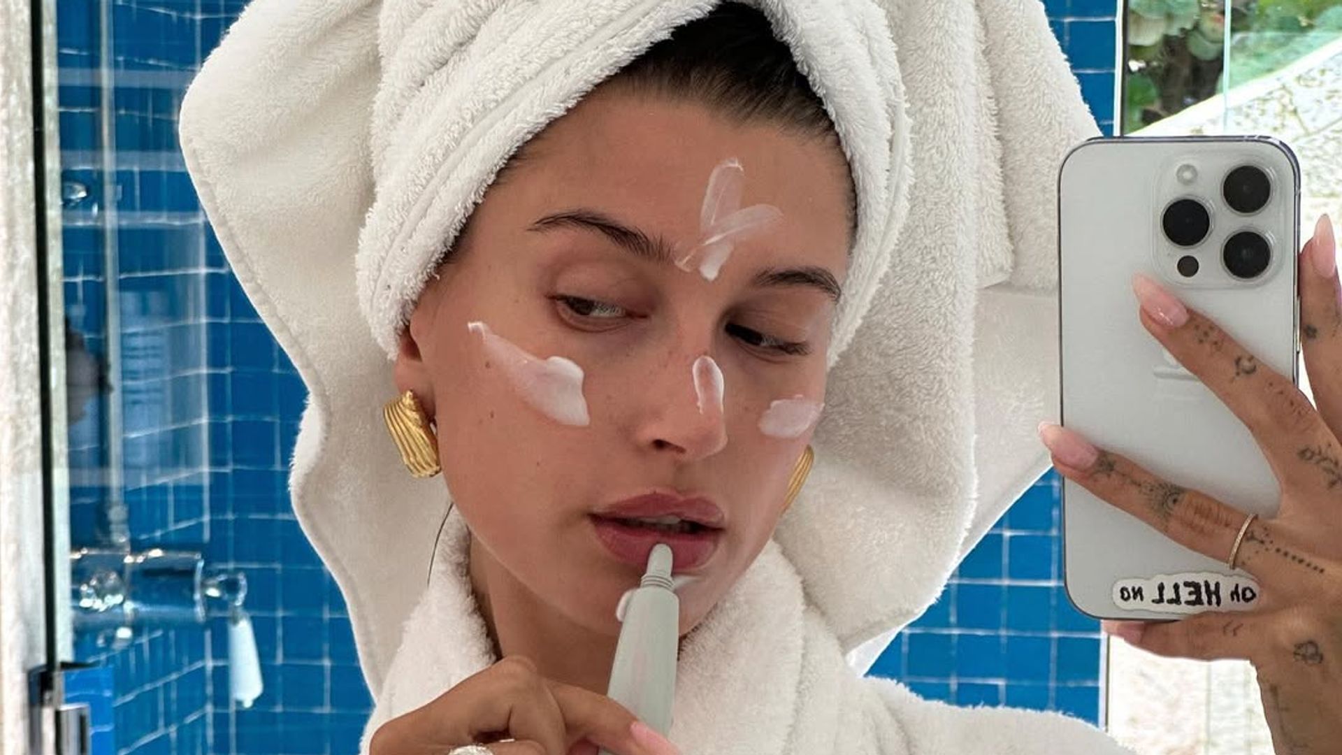 hailey bieber wearing towel applying skincare.