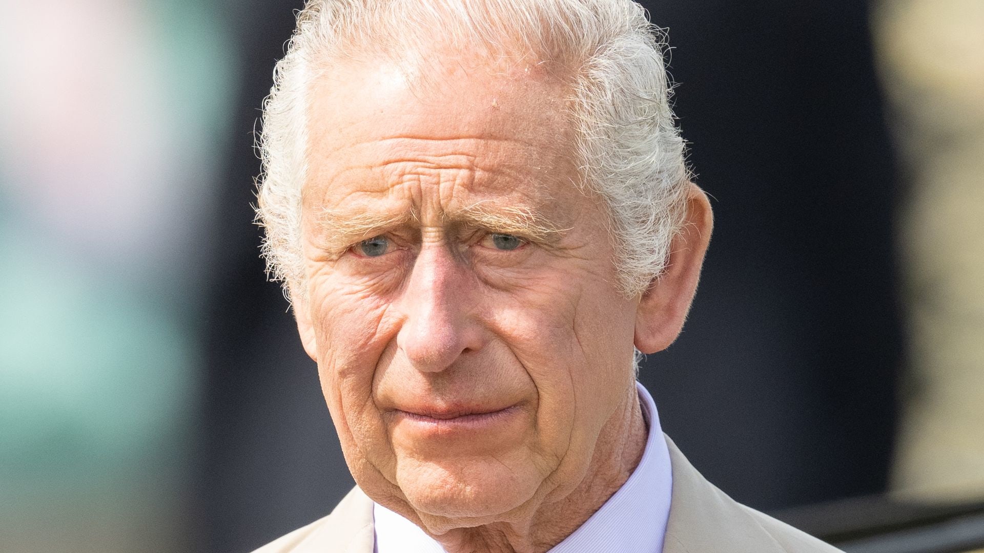 King Charles frowning in the sunshine in a cream suit