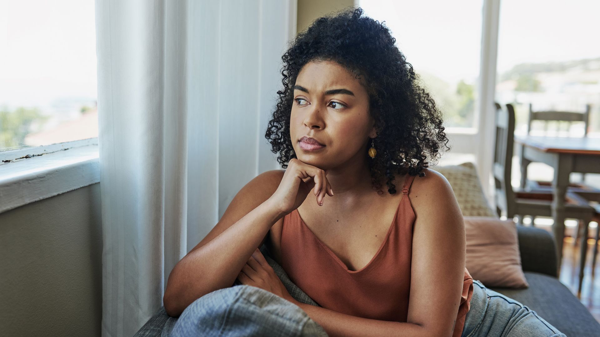 Shot of a young woman looking pensively out a window at home