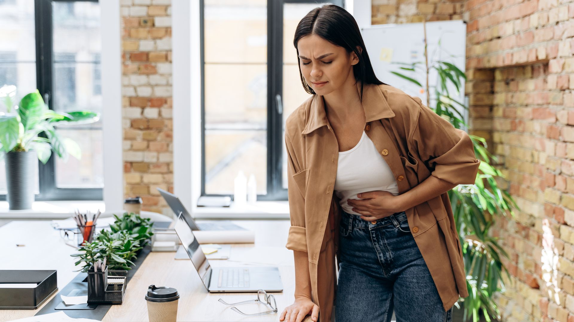 woman in an office holding her stomach and looking in pain