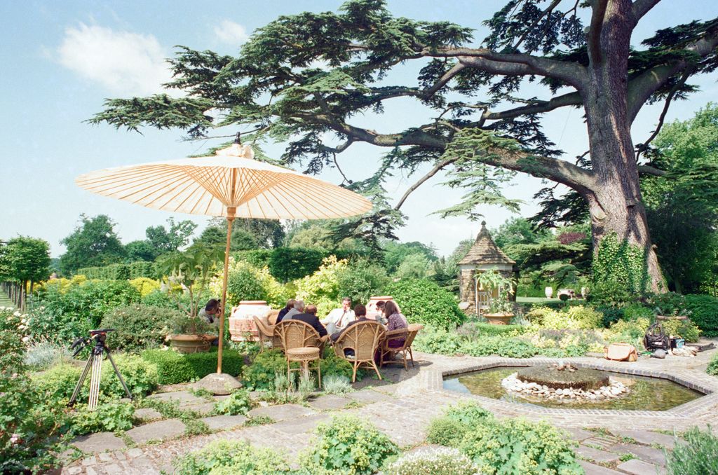 Highgrove gardens with large tree, with King Charles and press sitting around an outdoor table