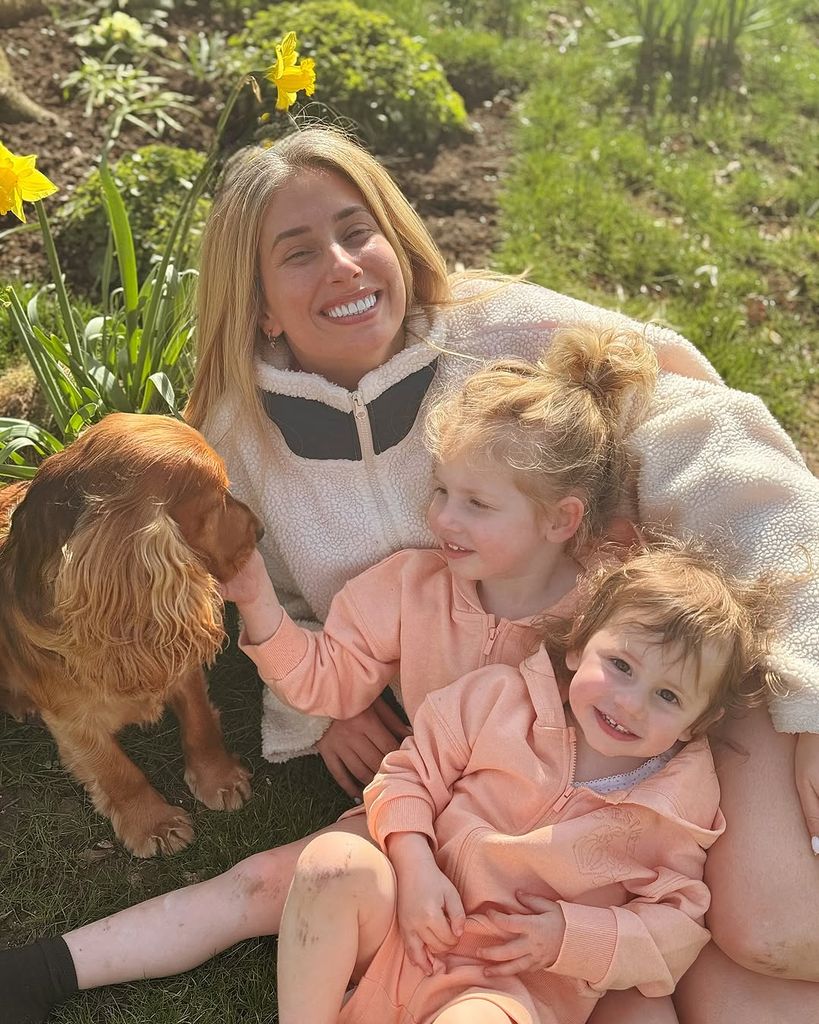 Stacey Solomon tersenyum di kebunnya bersama kedua putrinya, Belle dan Rose, duduk di pangkuannya sambil membelai kokspaniel hewan peliharaan mereka