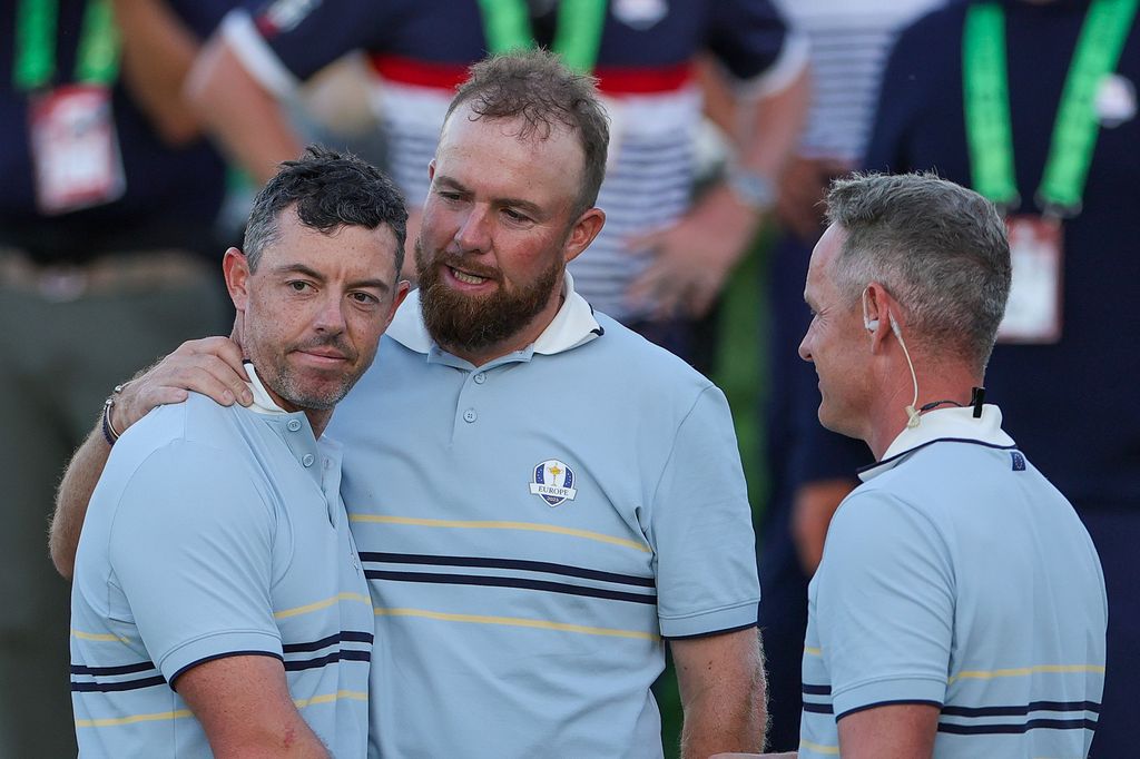 Shane Lowry of Team Europe hugs teammate Rory McIlroy as they talk to Captain Luke Donald of Team Europe after they tied their match with Patrick Cantlay and Sam Burns of Team United States during the Friday afternoon four-ball matches of the 2025 Ryder Cup at Black Course at Bethpage State Park Golf Course on September 26, 2025 in Farmingdale, New York