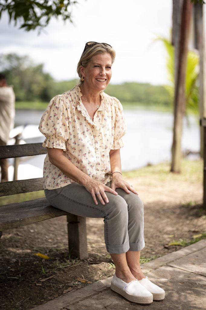 Duchess of Edinburgh duduk di luar di bangku mengenakan celana kargo dan blus bermotif bunga