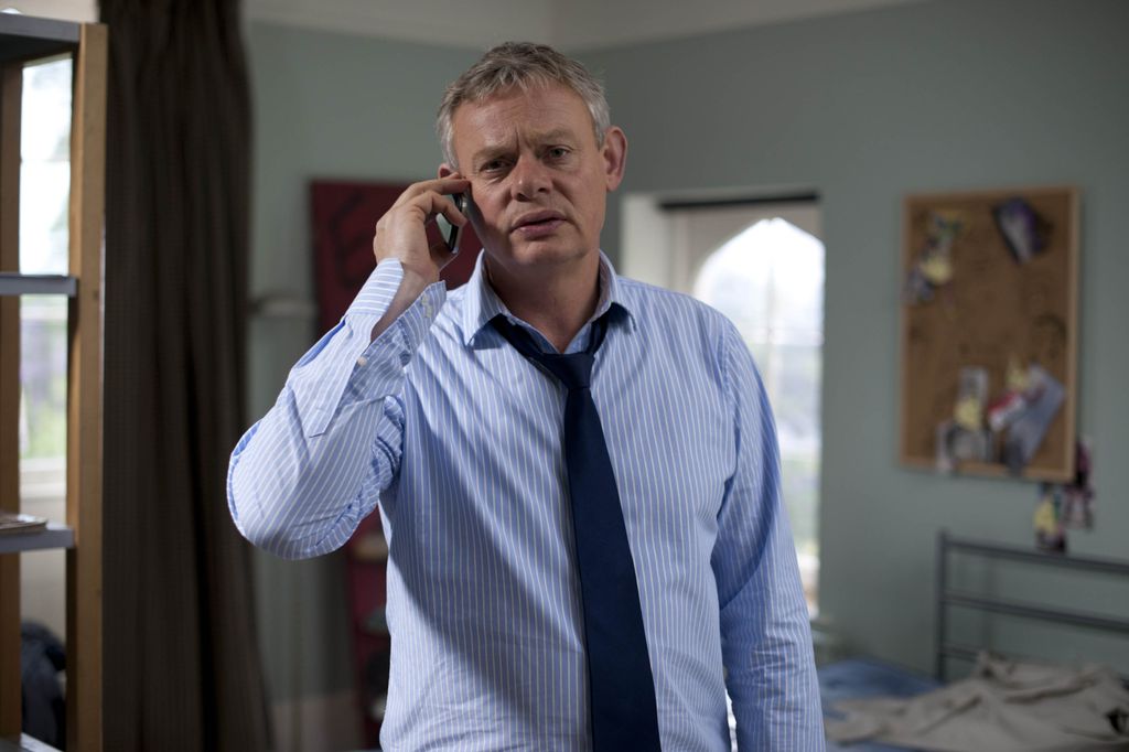 man in shirt and tie standing in bedroom holding mobile phone 