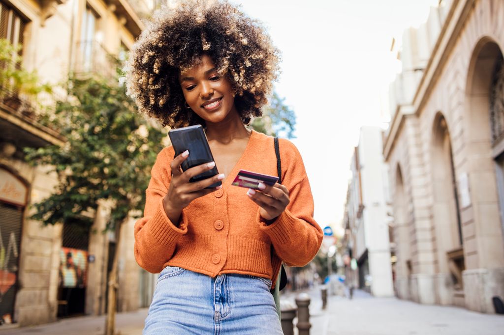 woman on vacation walking through Barcelona holding her phone and credit card