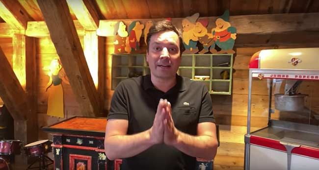 jimmy stands with his palms pressed together next to a popcorn maker with more brightly colored contraptions in the background