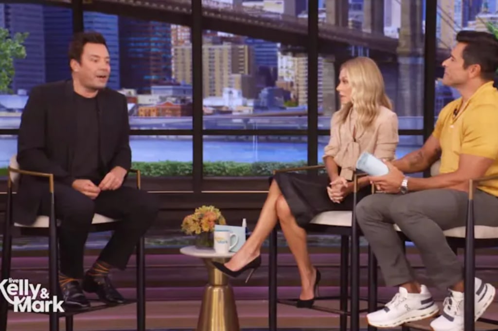 Jimmy Fallon in black blazer on LIVE with Kelly & Mark sat next to Kelly Ripa in black skirt and cream blouse and Mark Consuelos in yellow polo and gray pants