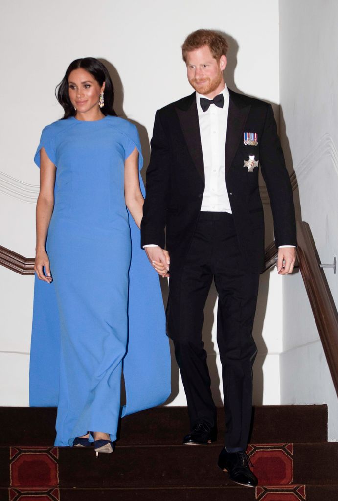 Prince Harry, Duke of Sussex in suit and Meghan, Duchess of Sussex in blue gown descending steps