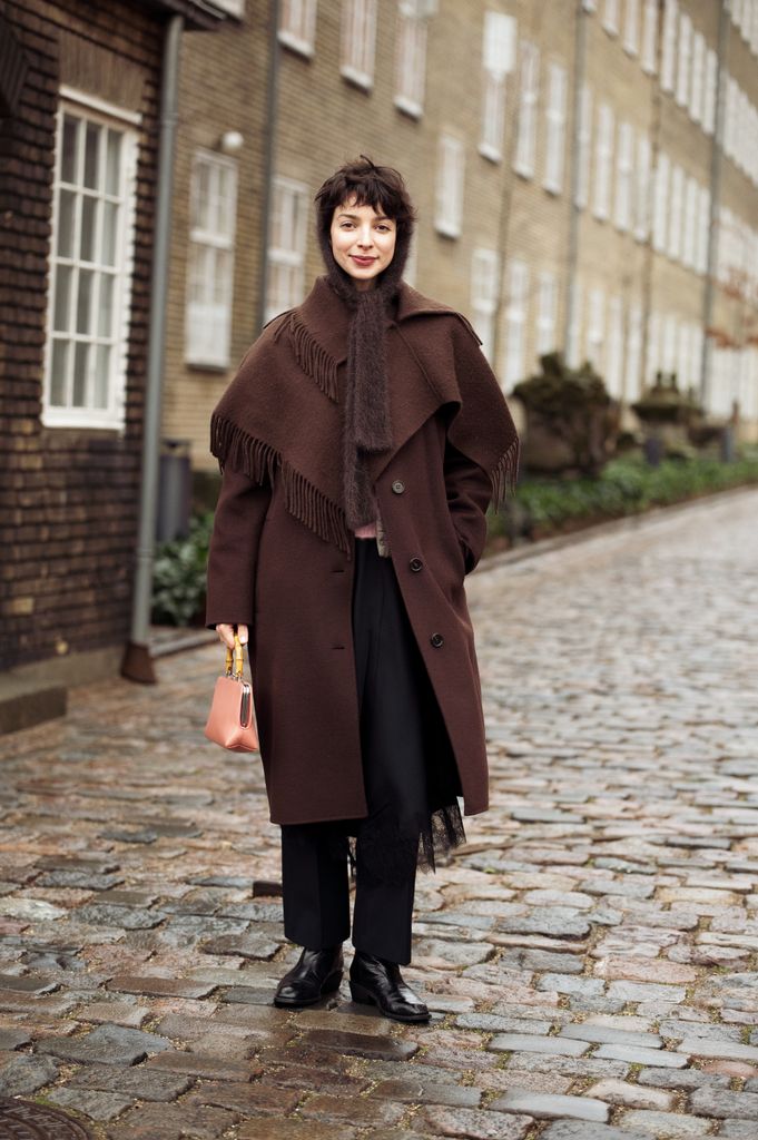 Katerina Chekan mengenakan celana hitam, mantel panjang coklat dengan jumbai, topi rajutan coklat dan tas merah muda peach ringan di luar acara OpÃ © Rasport selama Copenhagen Fashion Week Musim Gugur/Musim Dingin 2025 pada 27 Januari 2025 di Kopenhagen, Denmark