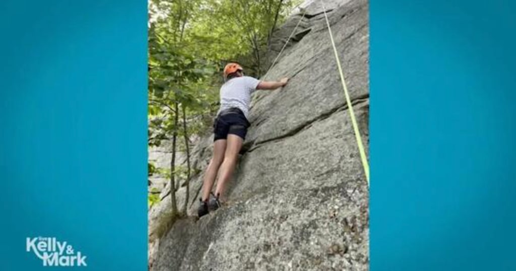 Jimmy Fallon in black shorts and gray t-shirt rock climbing