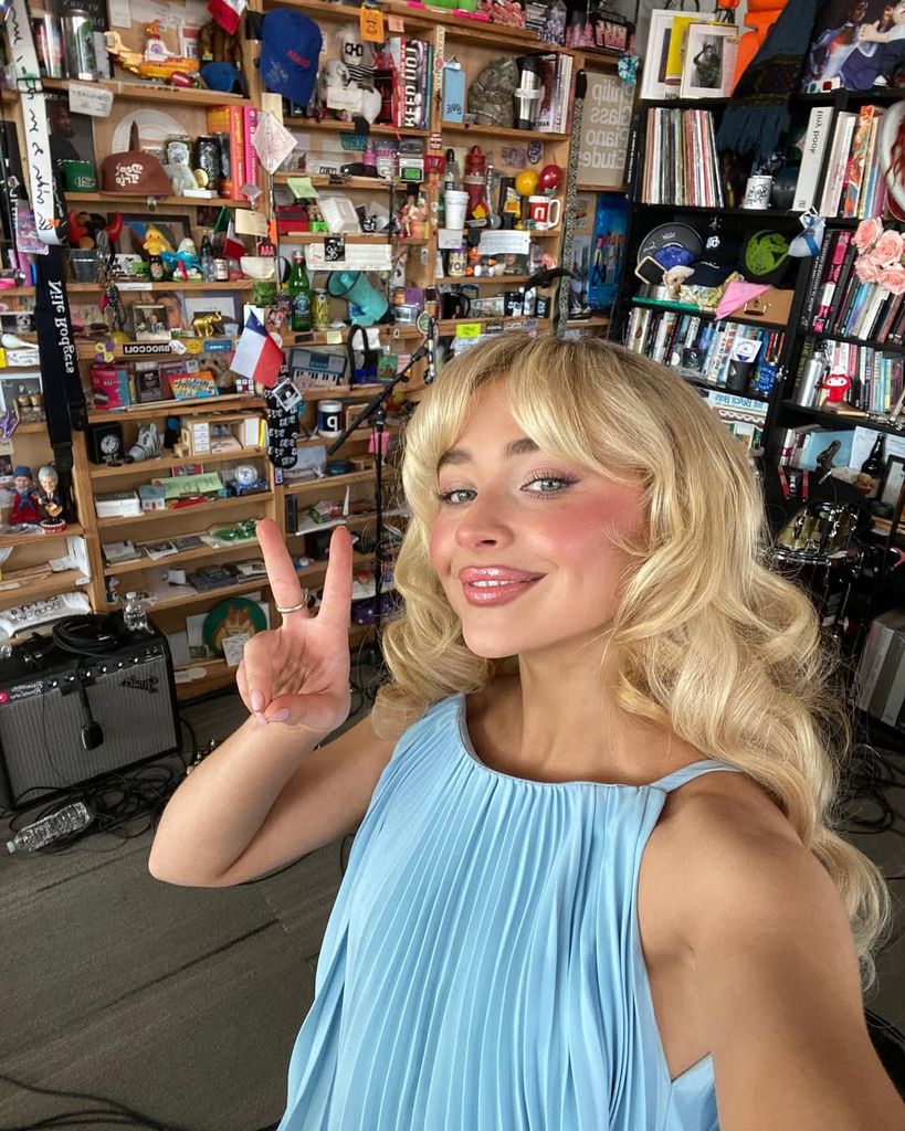 Sabrina Carpenter posing for selfie in blue dress with blonde curly hair