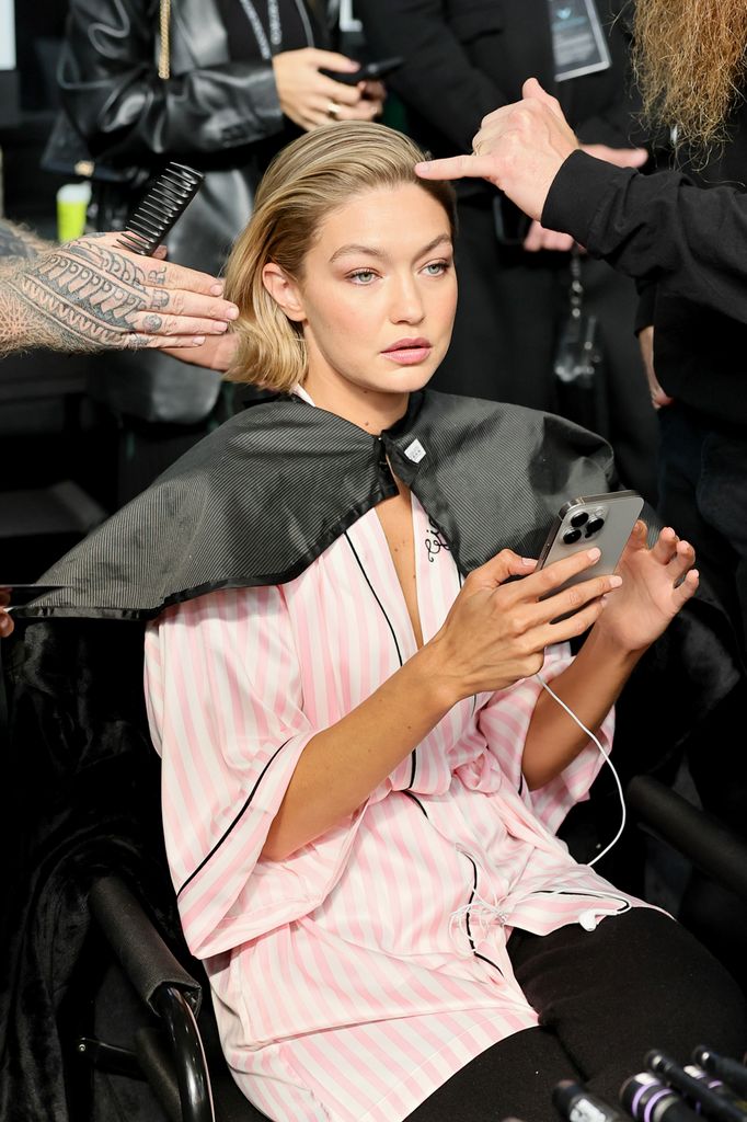 Gigi Hadid tampil tenang dan fokus saat stylist menyempurnakan penampilannya. Dengan jubah bergaris merah muda dan ponsel di tangan, ia tetap tenang sebelum tampil di runway, menampilkan keseimbangan sempurna antara profesionalisme dan ketenangan di balik layar.