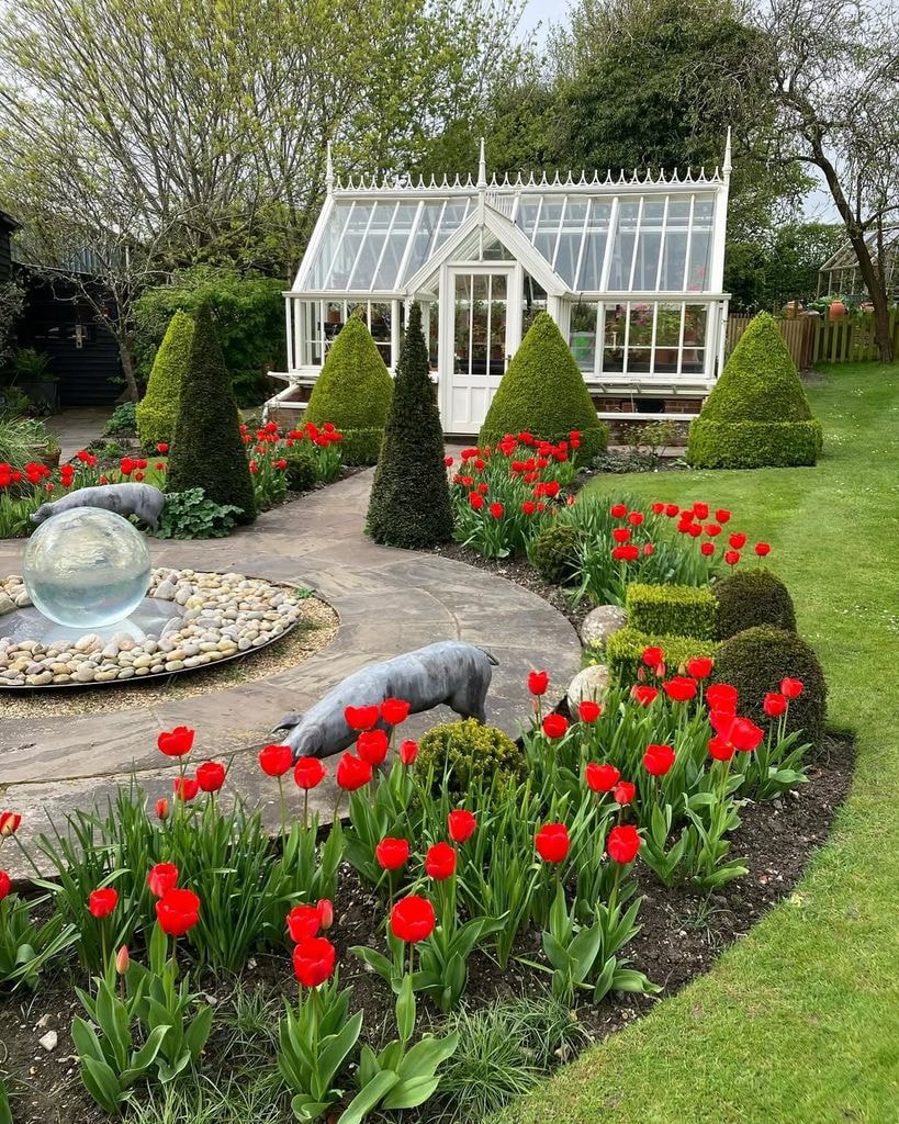 Exterior shot showing Alan Titchmarsh's greenhouse in his garden with water feature and bright red tulips