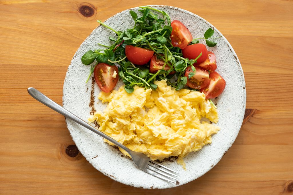 Scrambled eggs with tomato arugula salad on plate on wooden table. Healthy tasty breakfast omelette