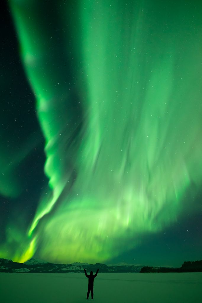 A silhouetted figure stands beneath an incredible northern lights display over Lake Laberge in Yukon.