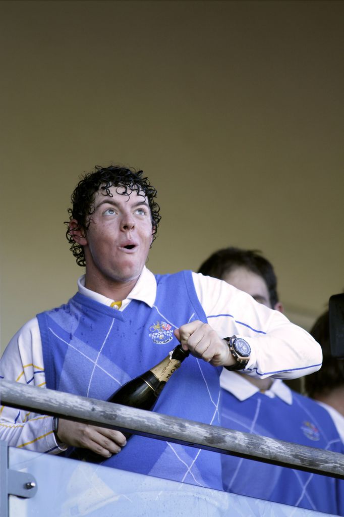   Rory McIlroy membuka sebotol sampanye mengenakan rompi sweter ungu yang dilapisi di atas kemeja polo putih yang renyah.