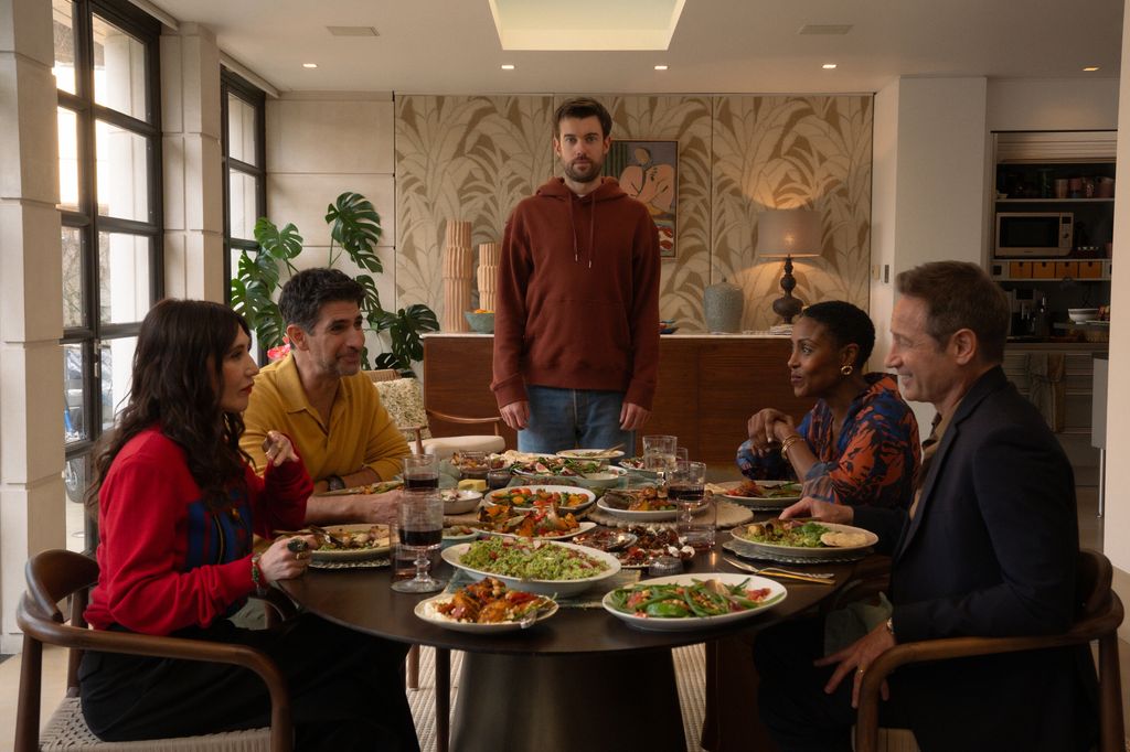 four people sitting at dinner table, man standing at head