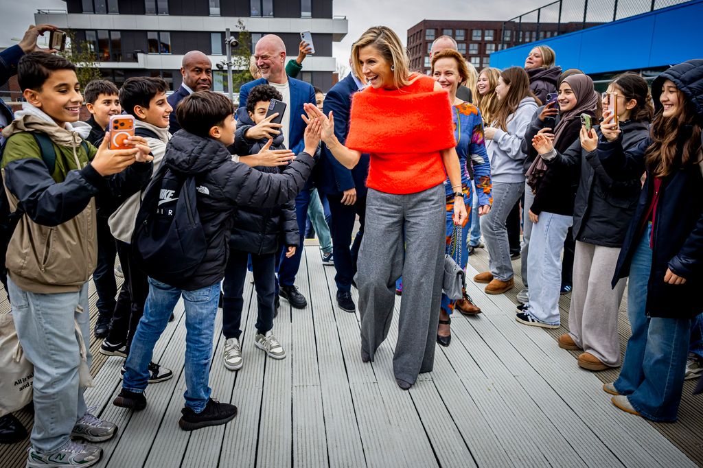 Queen Maxima high-fiving group of children in bright orange top and grey trousers