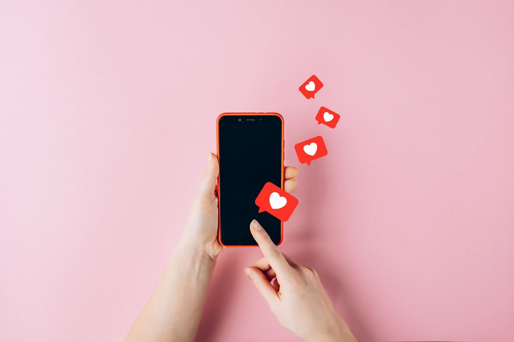 Female hands holding red mobile phone with many social media likes on pink background.