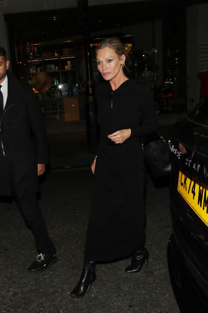 Kate Moss wearing a long black dress and black boots with her hair off her face