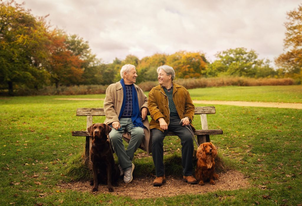 two older men sitting on park bench with dogs at their feet