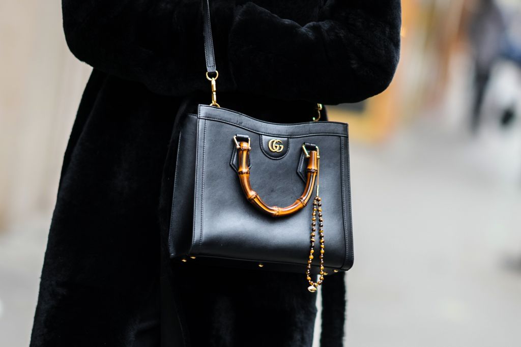 A guest wears a black fur long coat, a black shiny leather Diana crossbody bag from Gucci, outside Alexis Mabille, during Paris Fashion Week 2022