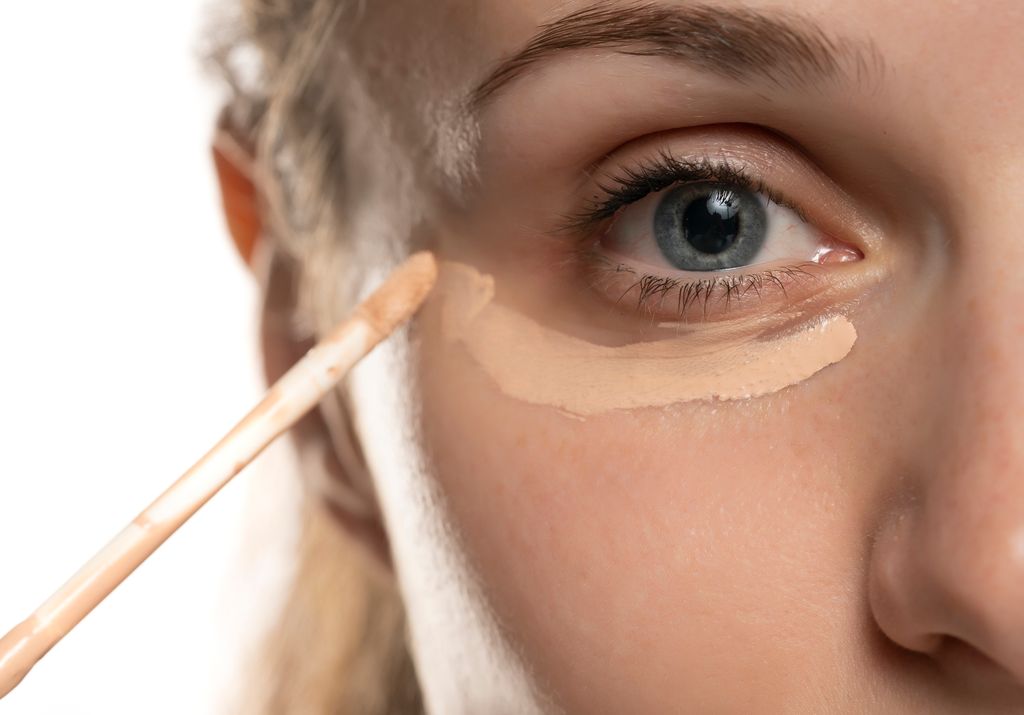 Closeup of a young woman applying concealer under her eye