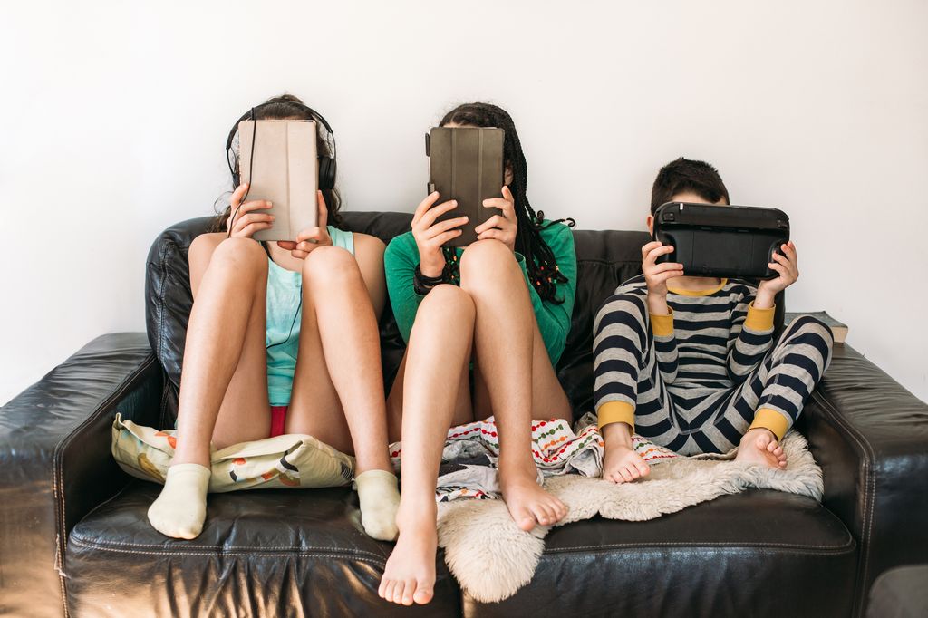 three kids on iPads on a sofa