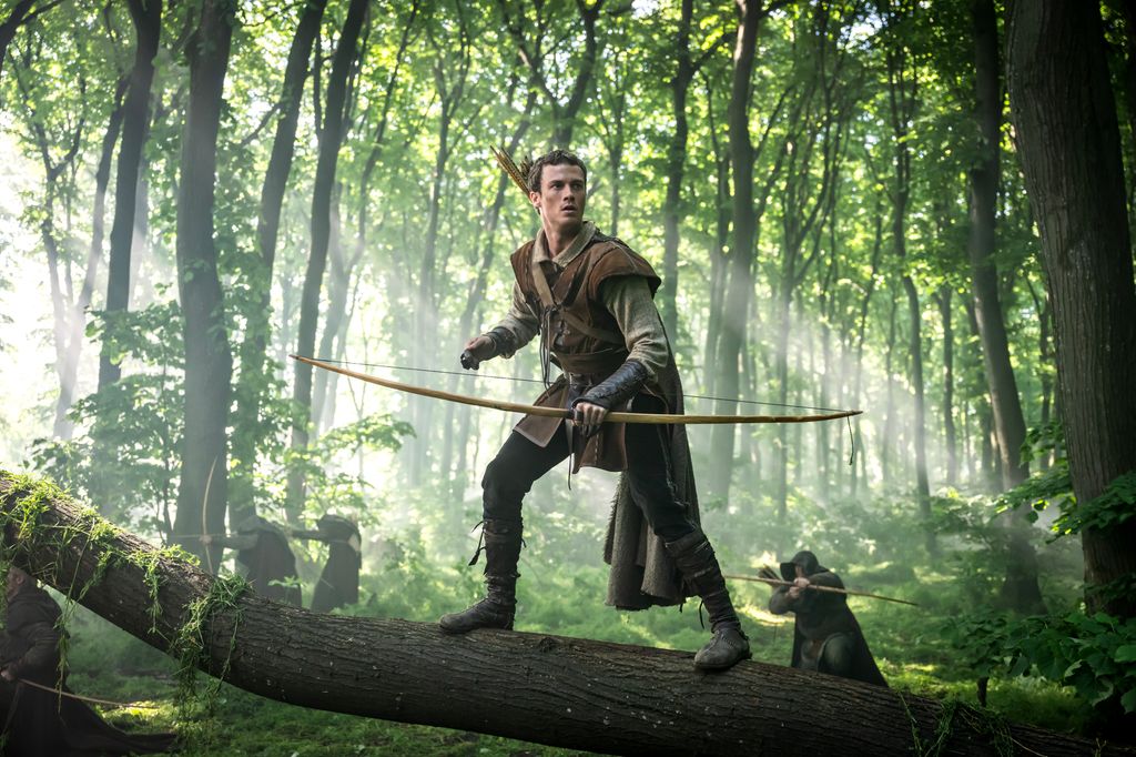 man standing on tree log holding bow and arrow