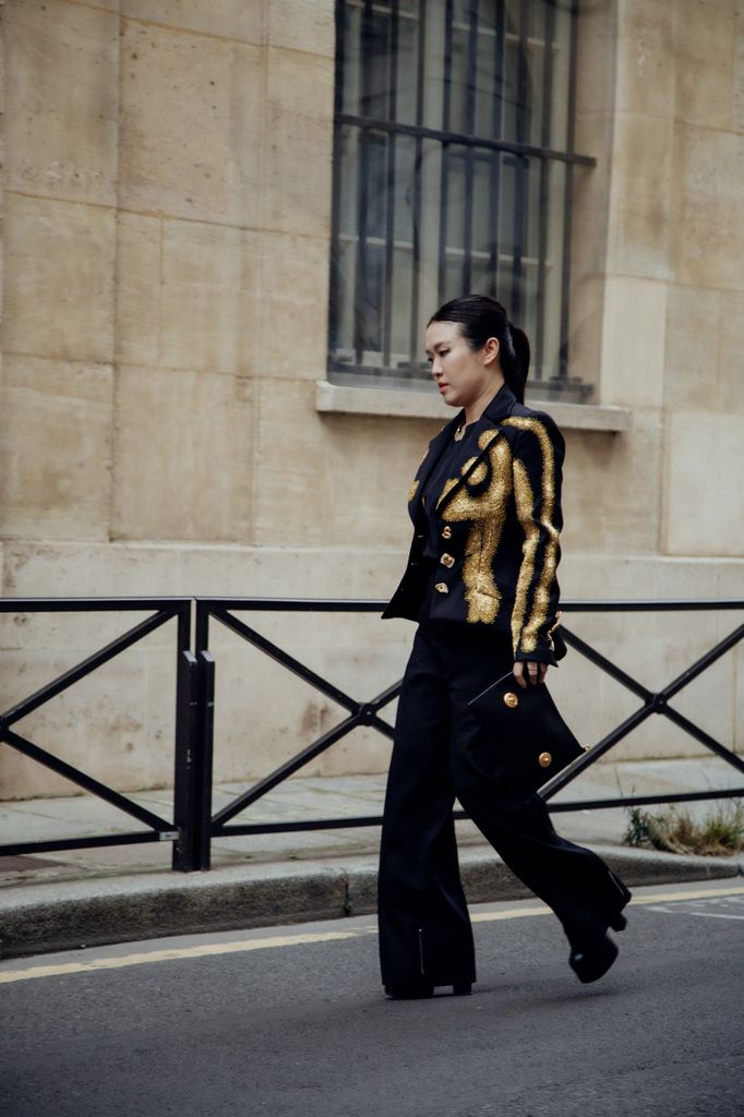 A guest wears black beaded trompe l'oeil Schiaparelli basque jacket, black trousers, boots on heels and on platform and a clutch during the Womenswear Spring/Summer 2024 as part of Paris Fashion Week on September 28, 2023 in Paris, France. (