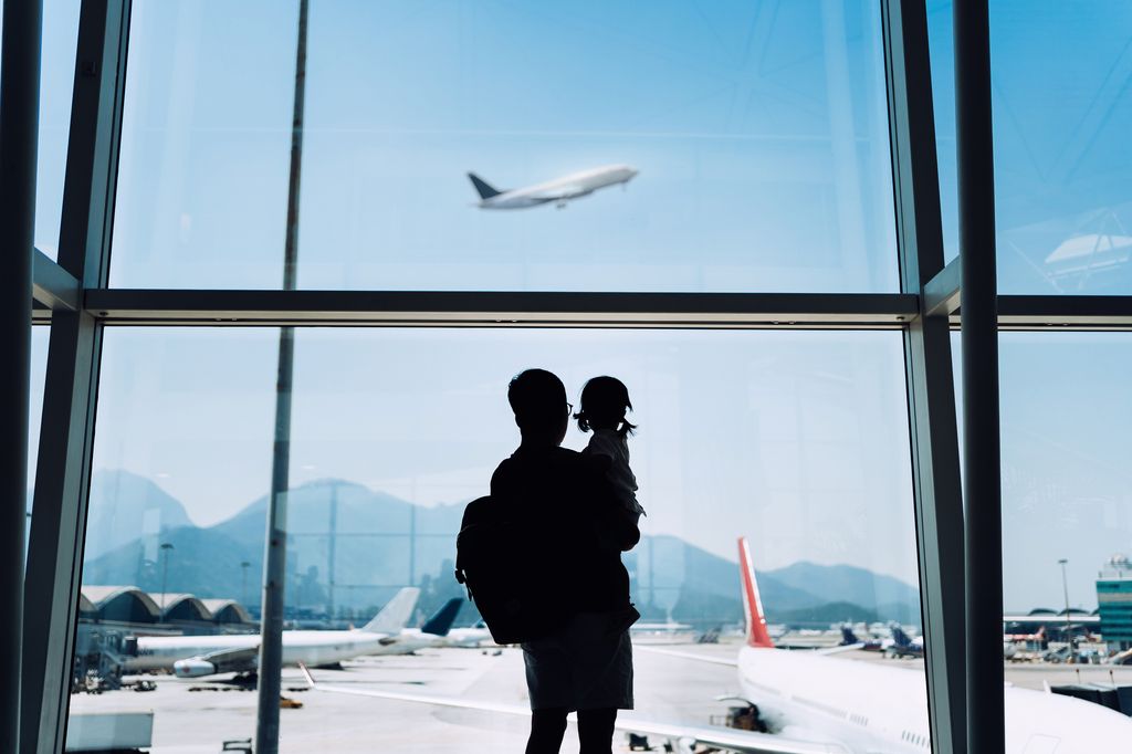 Silhouette of father carrying cute little daughter looking at airplane through window at the airport while waiting for departure