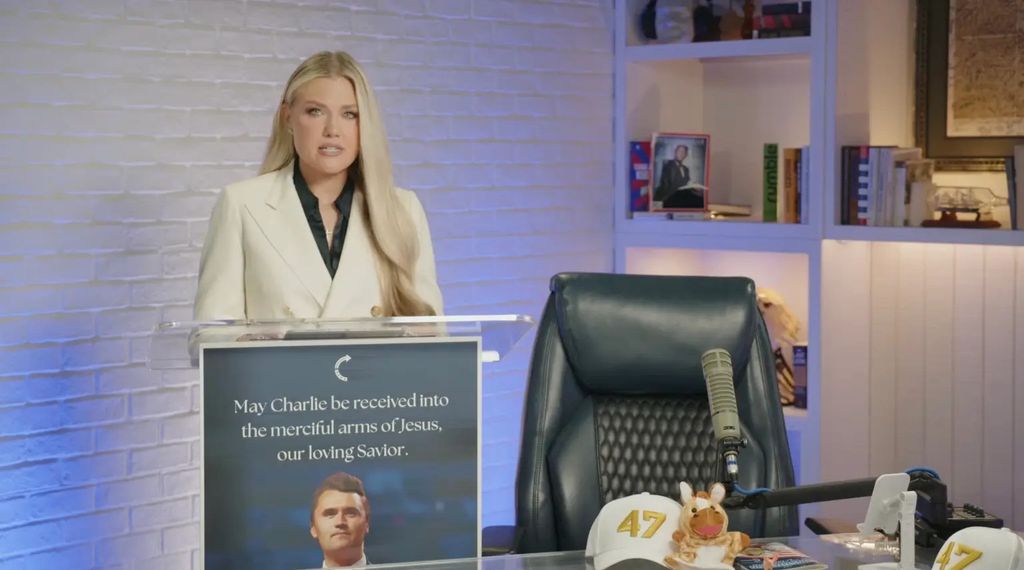 photo of erika kirk standing at a podium with charlie kirk face on addressing nation in speech on youtube