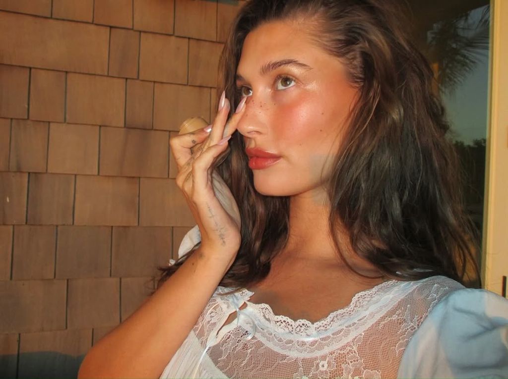 Selfie of Hailey Bieber in white lace top applying blush