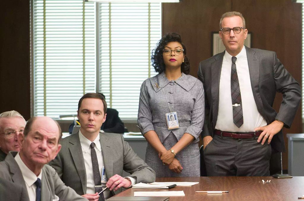Kevin Costner (far right) in Hidden Figures alongside Taraji P Henson (middle) and Jim Parsons (left). Jim is sat at a large desk and Taraji and Kevin are standing.