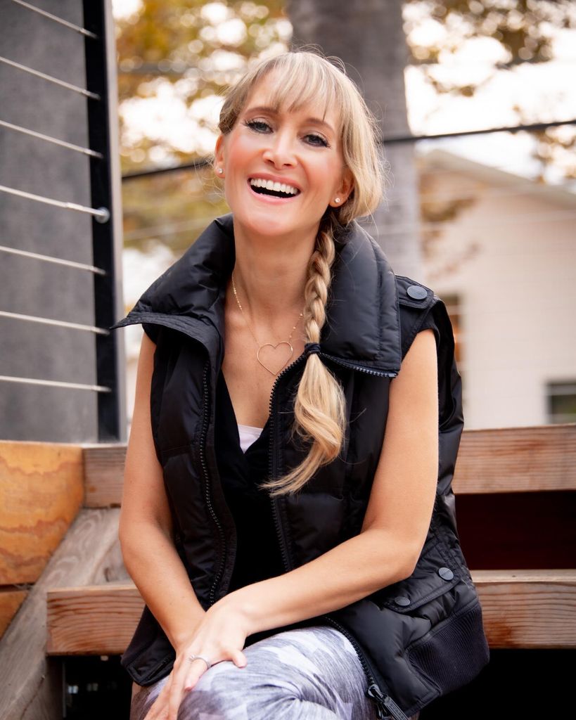 Jaime Bronstein laughing, sat on steps, wearing a black gilet 
