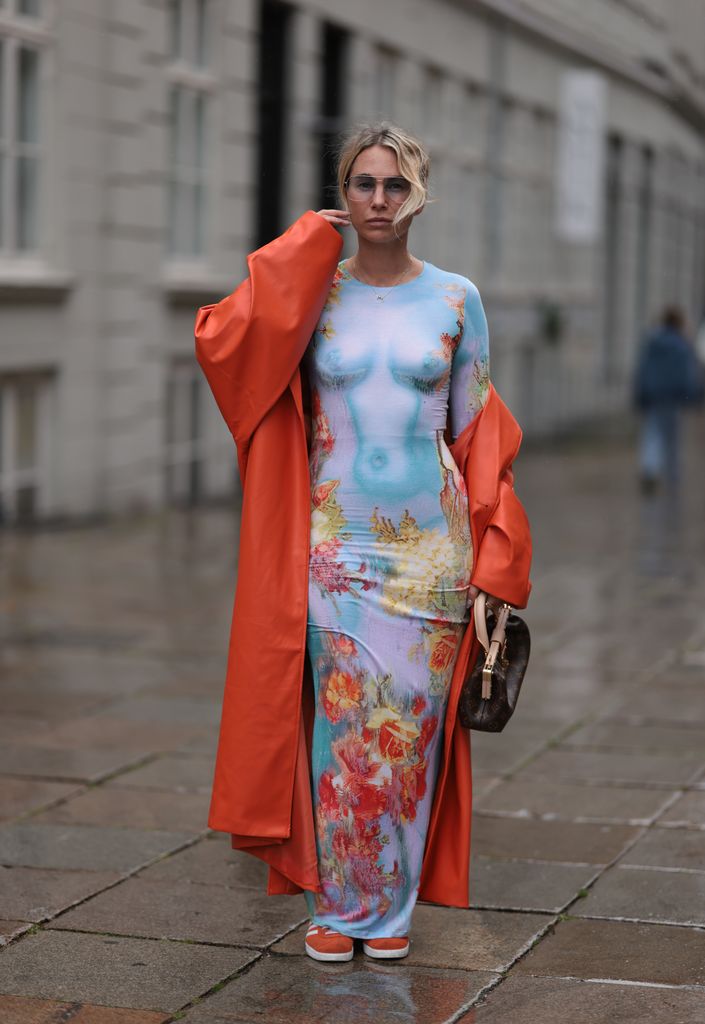 Karin Teigl seen wearing Jean Paul Gaultier light blue colorful print pattern long dress, Andy Wolf light blue transparent pilot sunglasses, NA-KD dark orange leather long coat, Louis Vuitton brown leather / logo pattern canvas handbag, Adidas orange suede leather Samba sneakers, during the Copenhagen Fashion Week